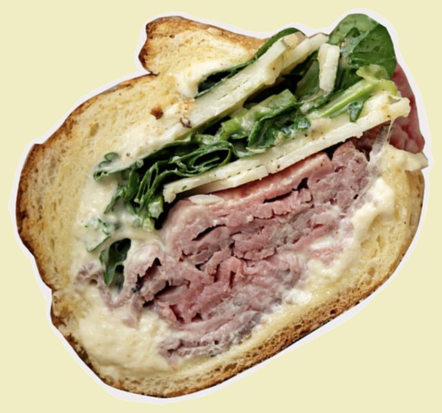 Cross-section of a roast beef sandwich with creamy dressing, greens, and cheese on toasted bread.
